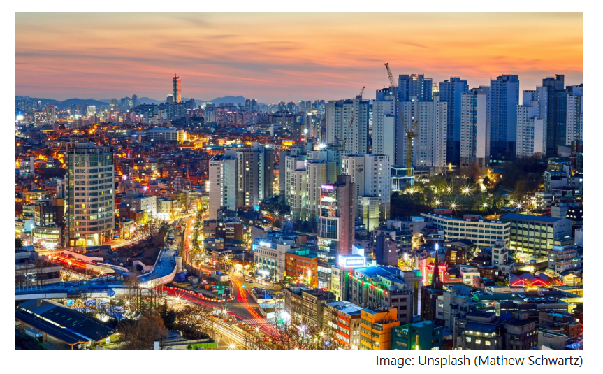 Seoul cityscape at dusk, with dense apartment towers and winding streets illuminated by evening traffic and city lights.
