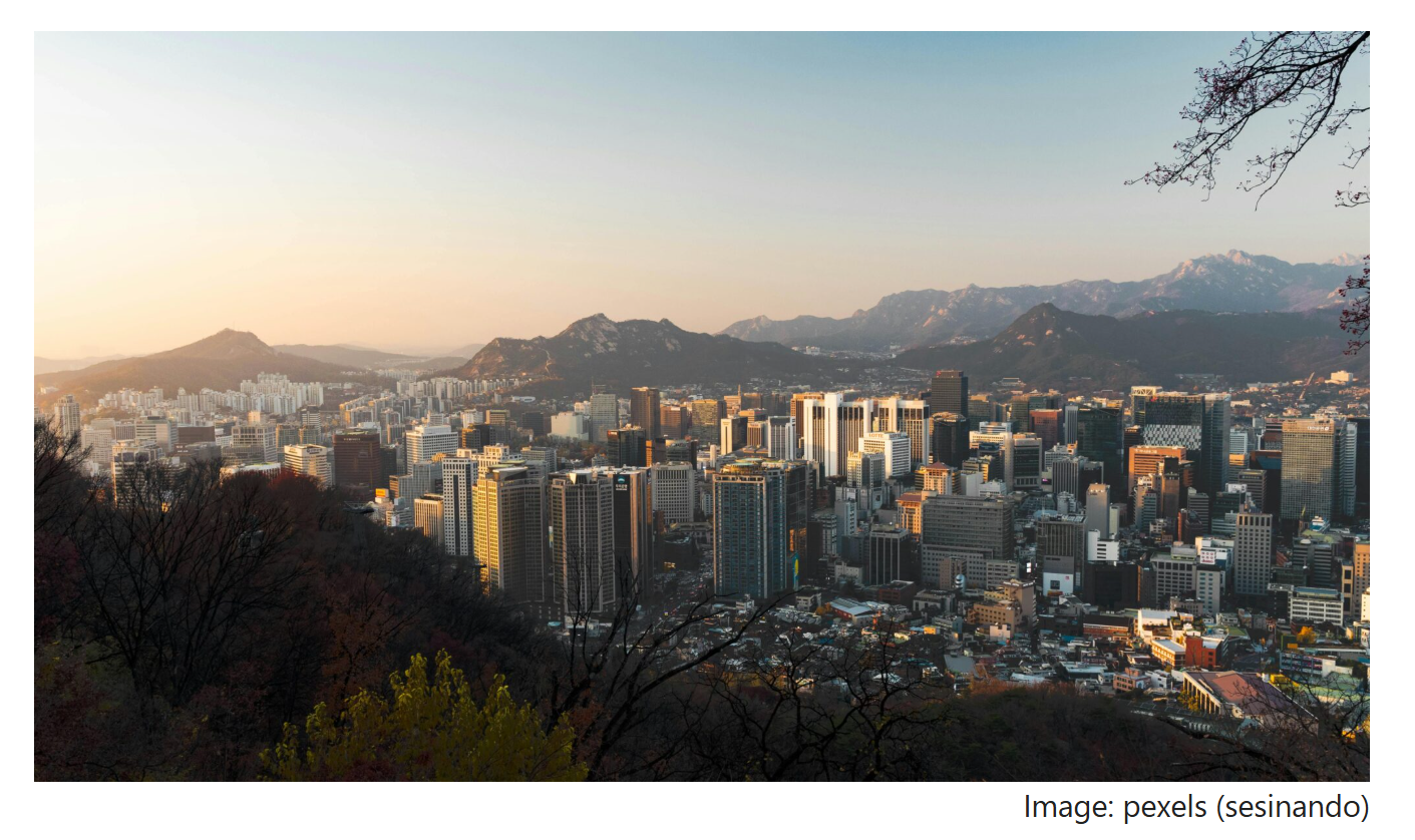 A view of central Seoul with high-rise buildings and distant mountain ridges, seen from an elevated viewpoint at sunset.
